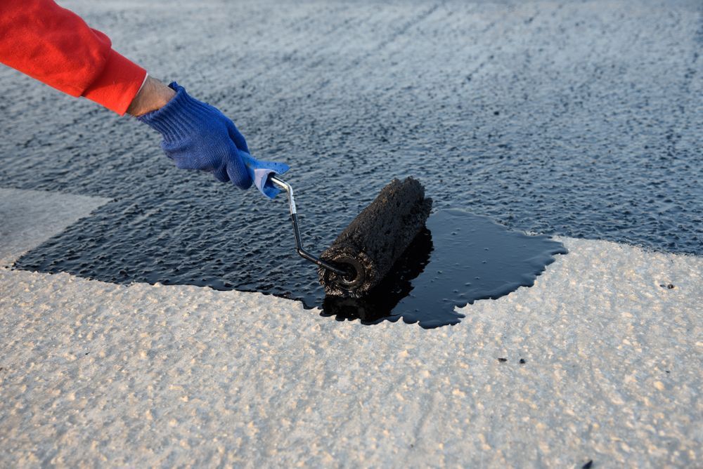Person in Blue Glove Rolls Black Sealant Onto a Light Gray Surface — 1 Time Waterproofing In East Ballina, NSW