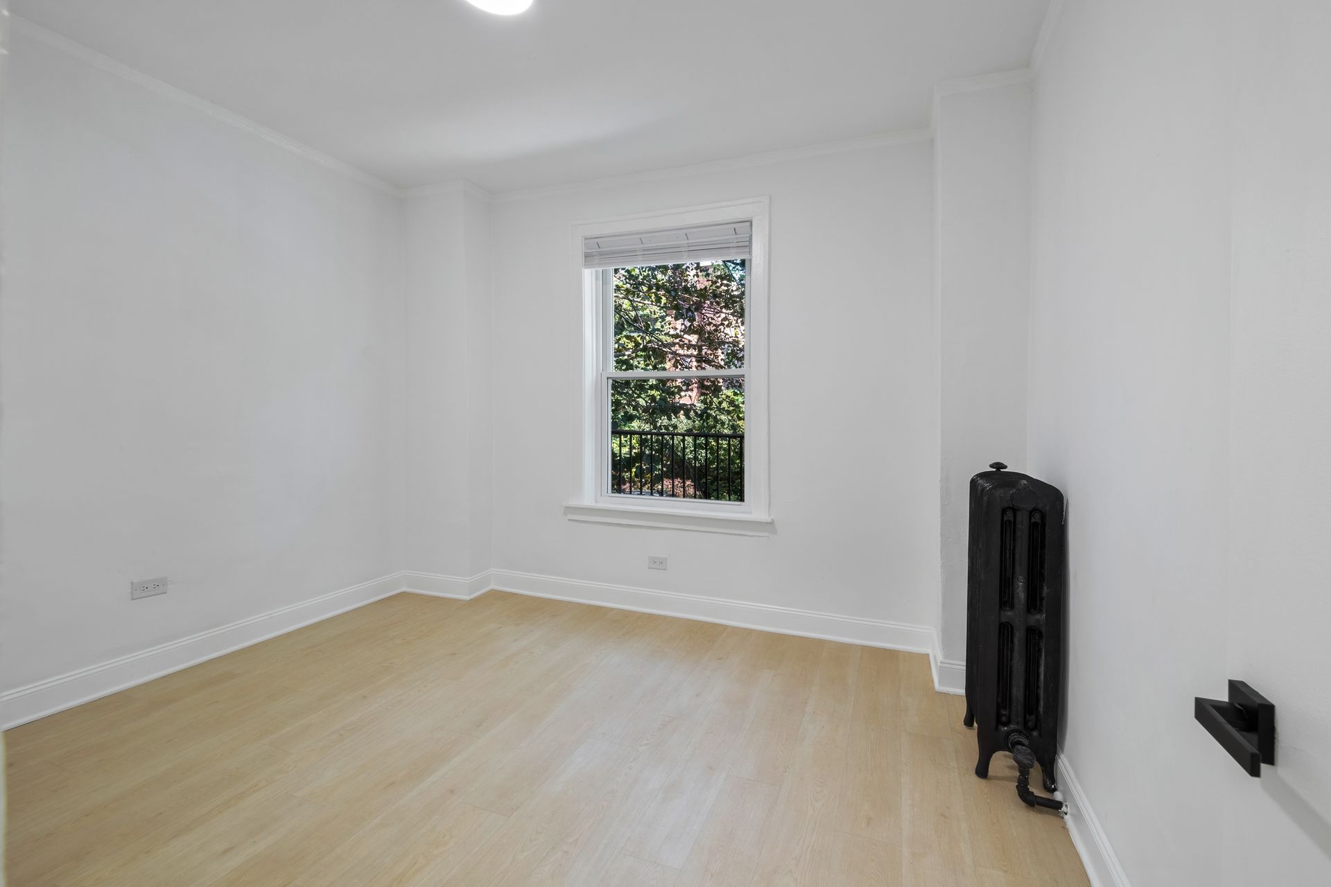 Empty white room with a window, hardwood floors, and a radiator.