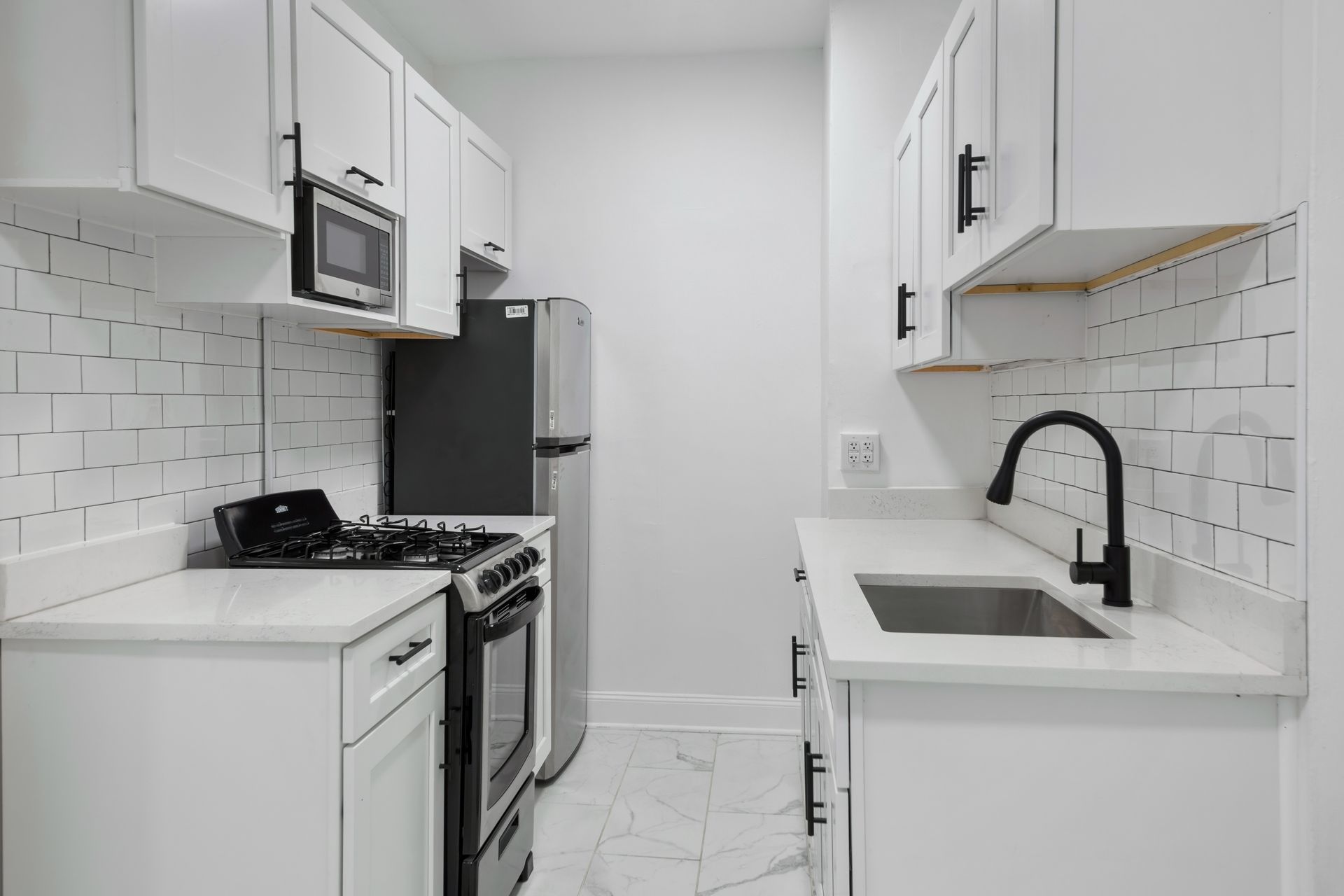 Small white kitchen with black appliances, subway tile backsplash, and black faucet.