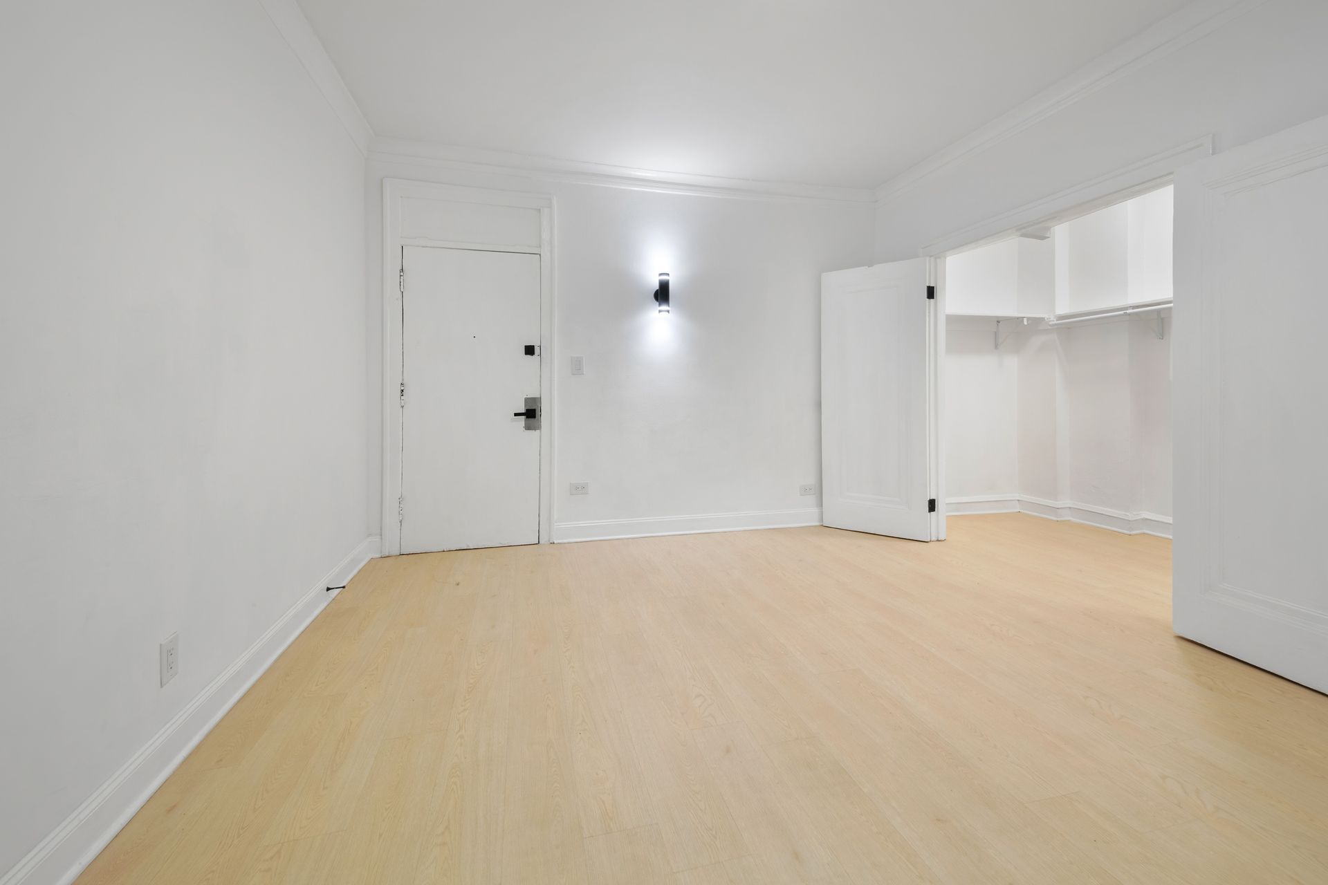 Empty room with light wood floor, white walls, a closet, and door.