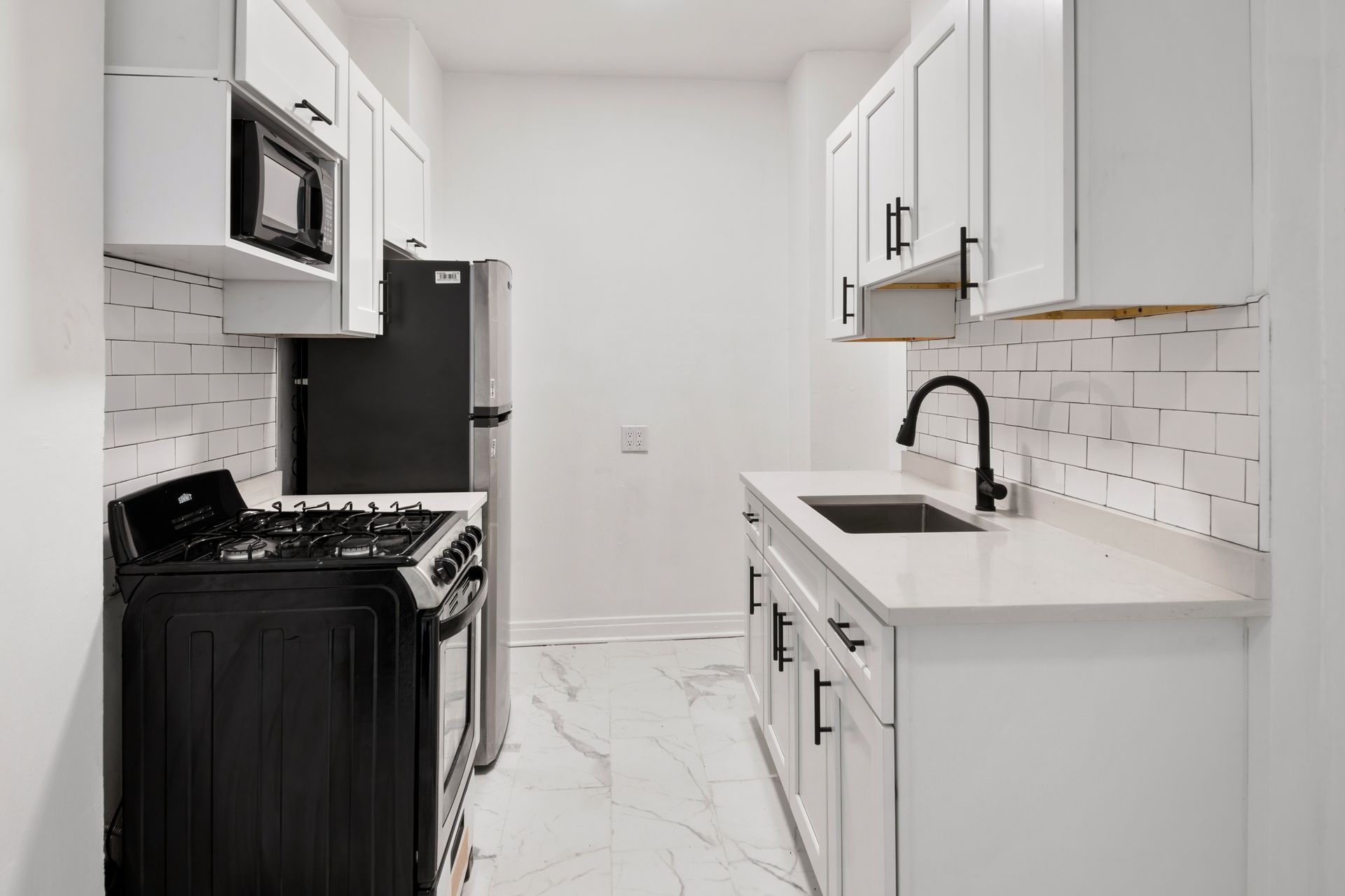 Small, modern white kitchen with black appliances, white countertops, and tiled backsplash.