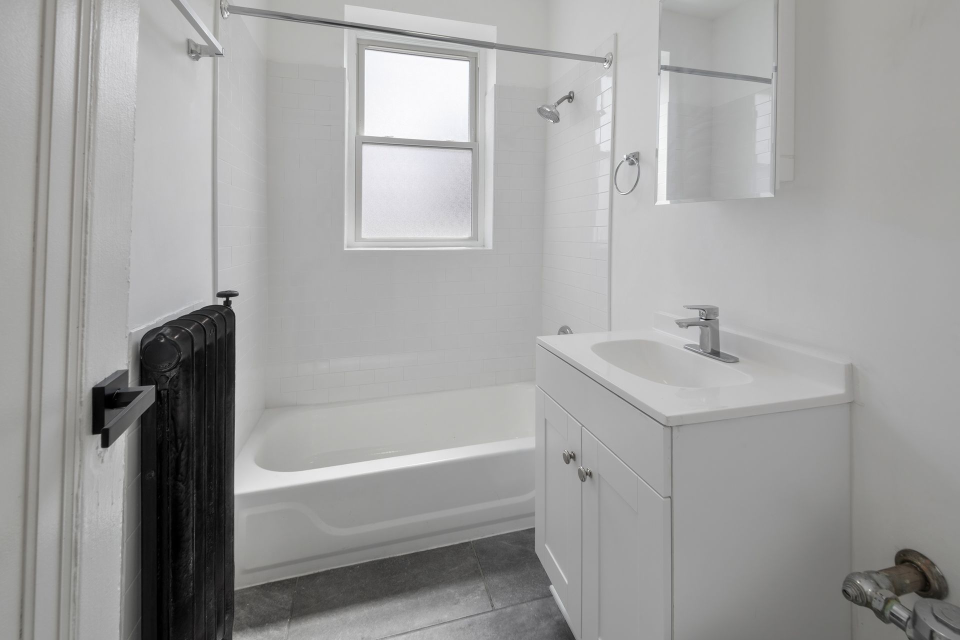 White bathroom with a tub, vanity, window, and black radiator.