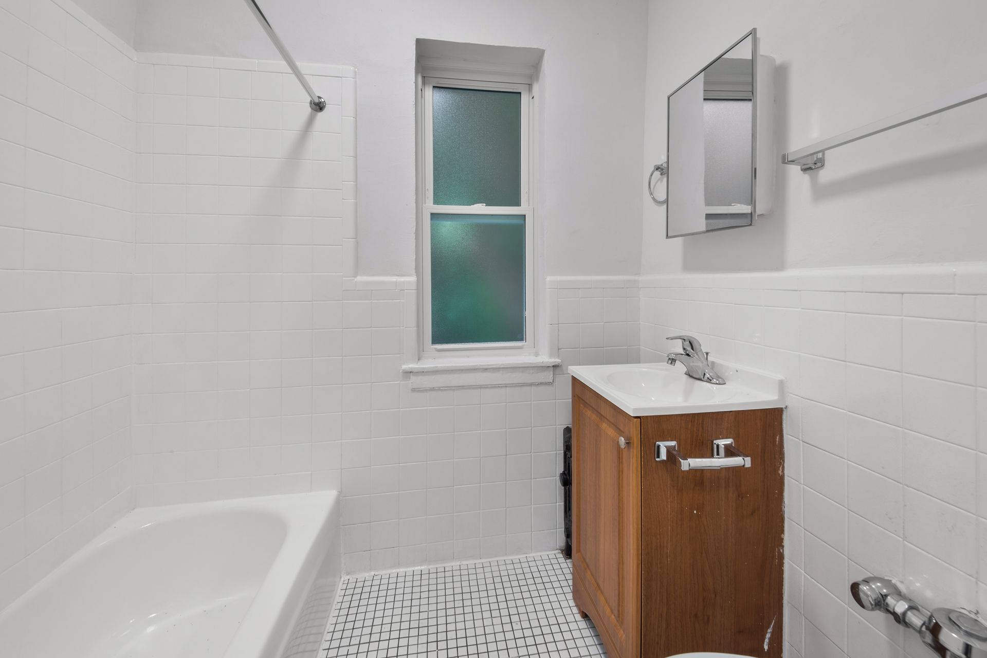 White tiled bathroom with tub, vanity, and small window.