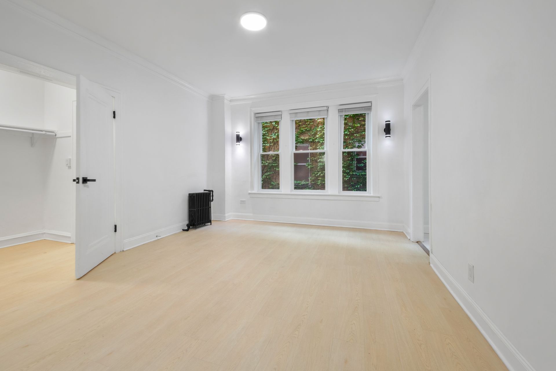 Empty white room with light wood floor, window, and open closet.