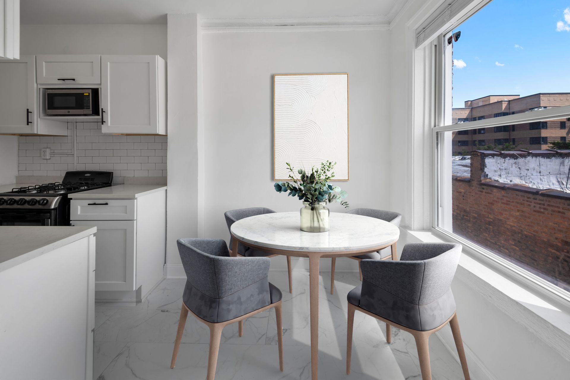Small white kitchen with a round table, four gray chairs, and a sunny window.