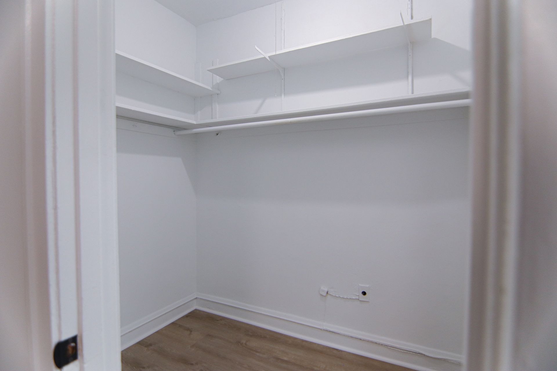 Empty white closet with shelves and rod; wood-look floor.