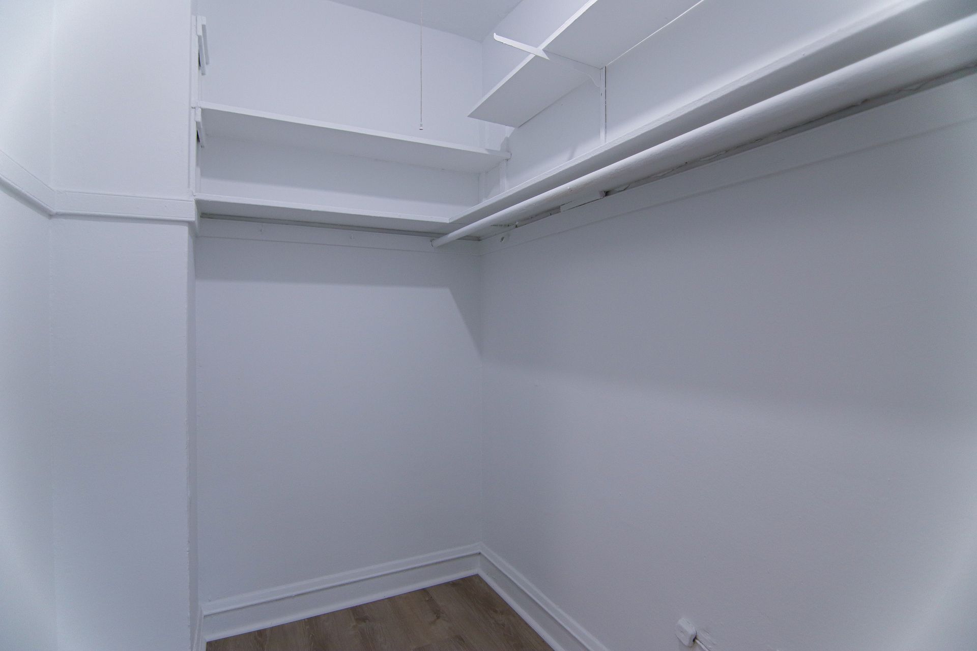 Empty white closet with shelves and a clothing rod; wood-look floor.