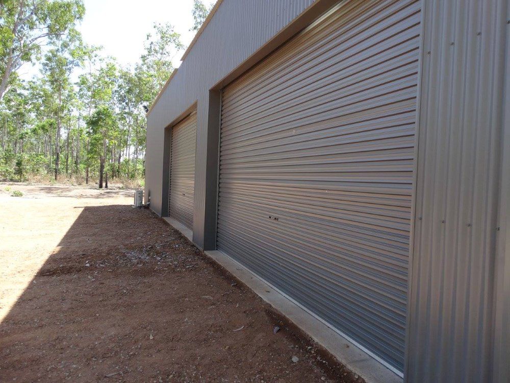 A Row Of Garage Doors On A Building With Trees In The Background — SLS Builders Pty Ltd in Yarralin, NT