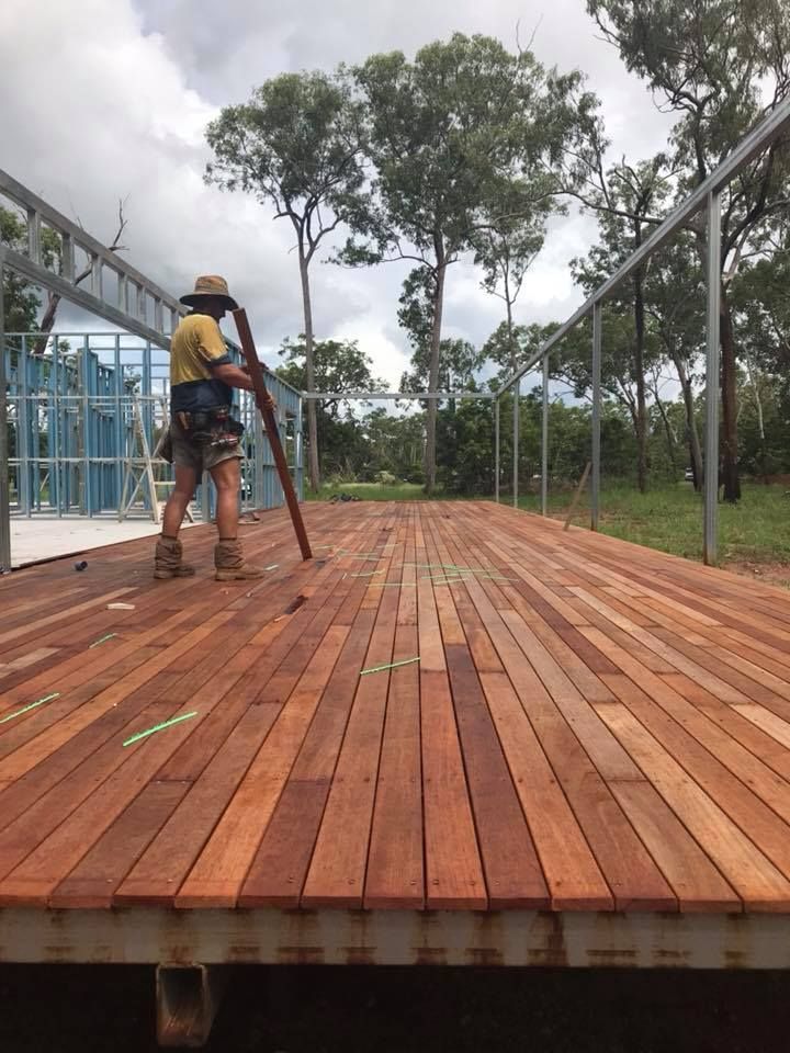A Man Is Standing On A Wooden Deck Holding A Pole — SLS Builders Pty Ltd in Yarralin, NT