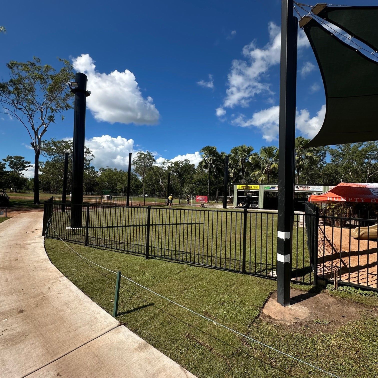 A park area with black fences, a paved path, green grass, and a bright blue sky with clouds — SLS Builders Pty Ltd in Humpty Doo, NT