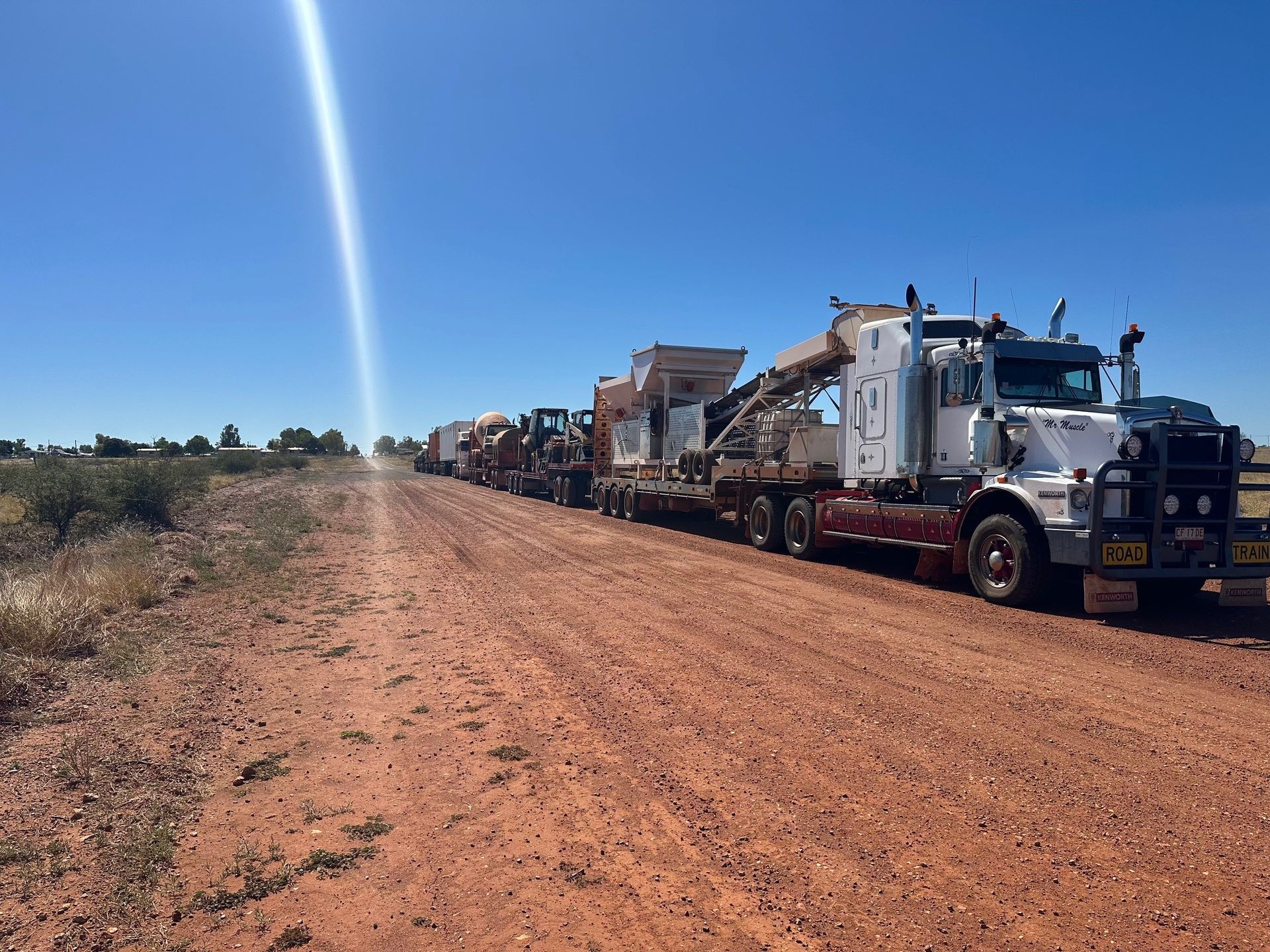 A long convoy of trucks on a dusty red road under a bright blue sky — SLS Builders Pty Ltd in Katherine, NT