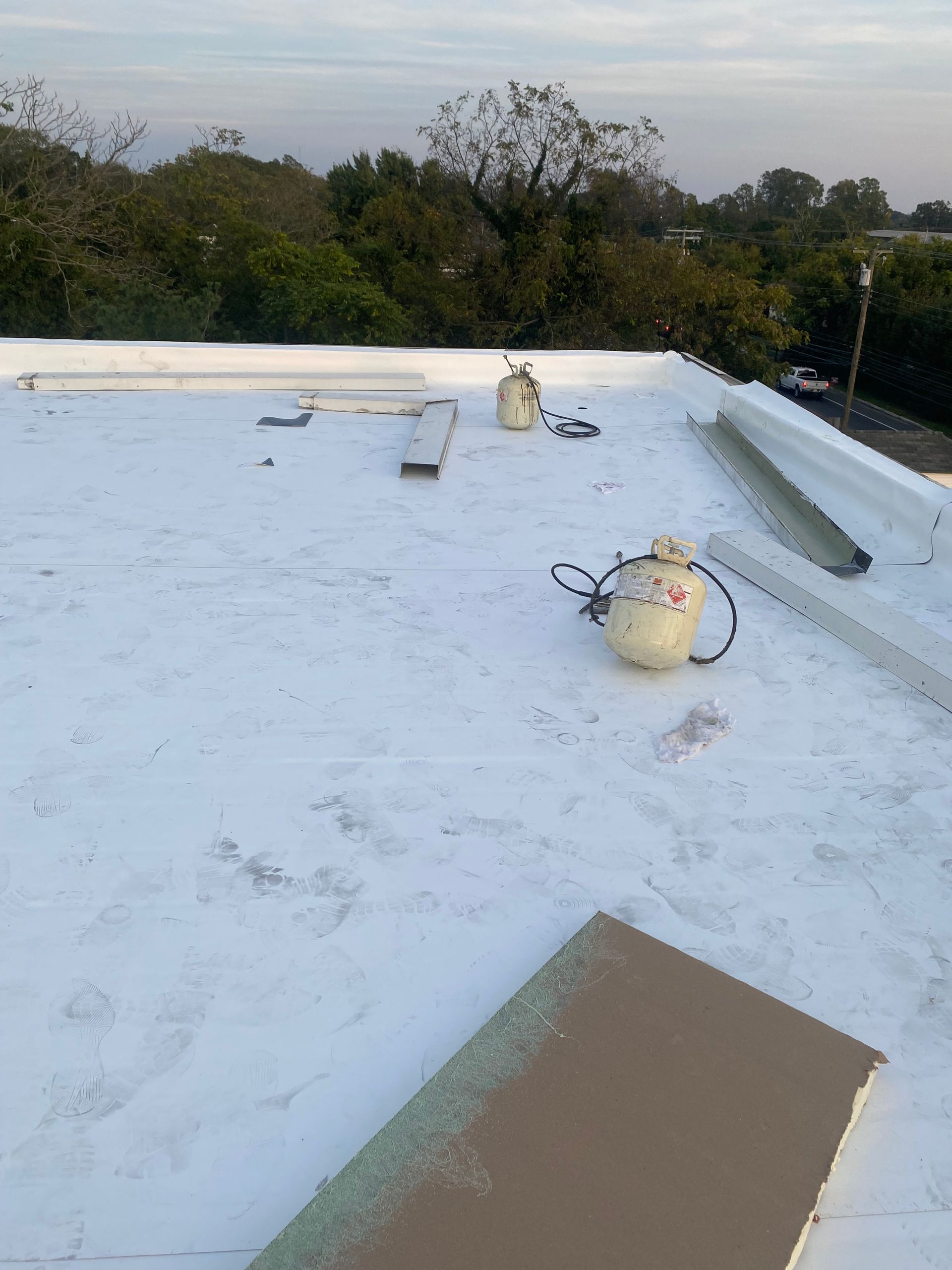 White rooftop with two buckets and a long board, trees visible in the background.