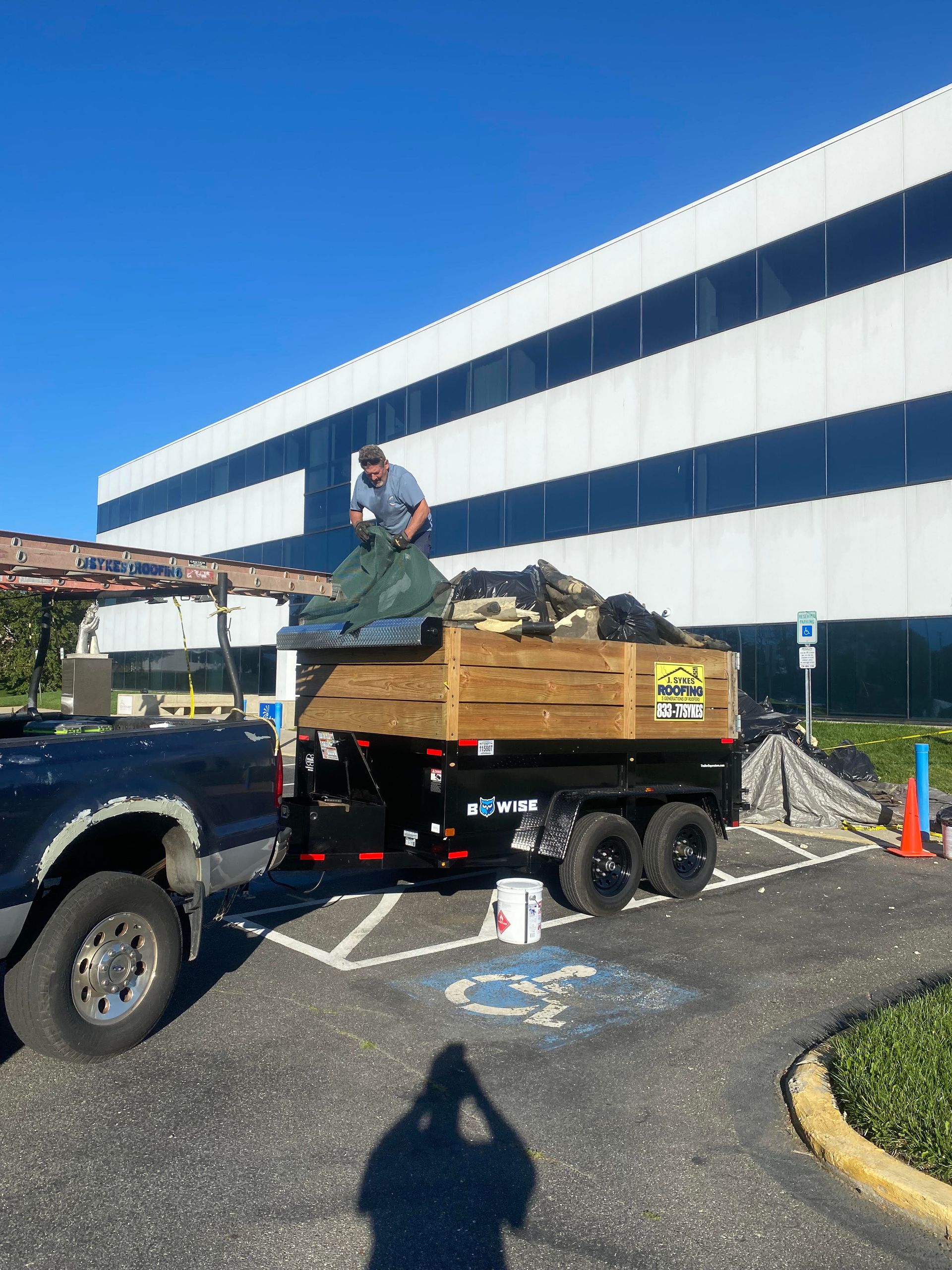 Worker on a flatbed truck loading debris outside a large white building on a sunny day