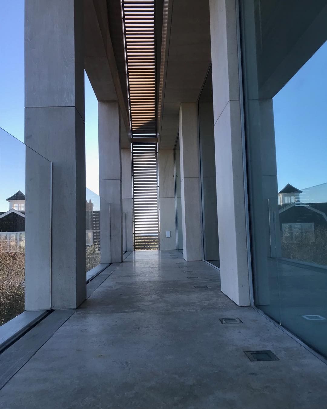 Walkway between concrete pillars with stairs in the distance. Blue sky and building exteriors visible.