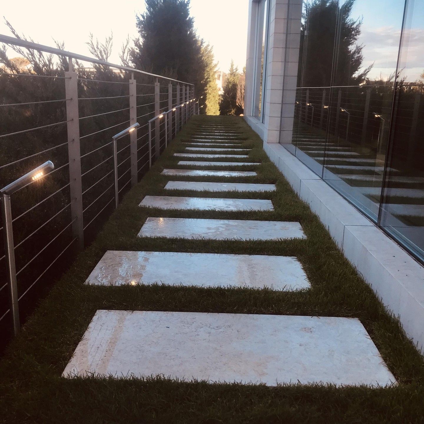 Stone path with grass in between, beside a building with a cable railing.
