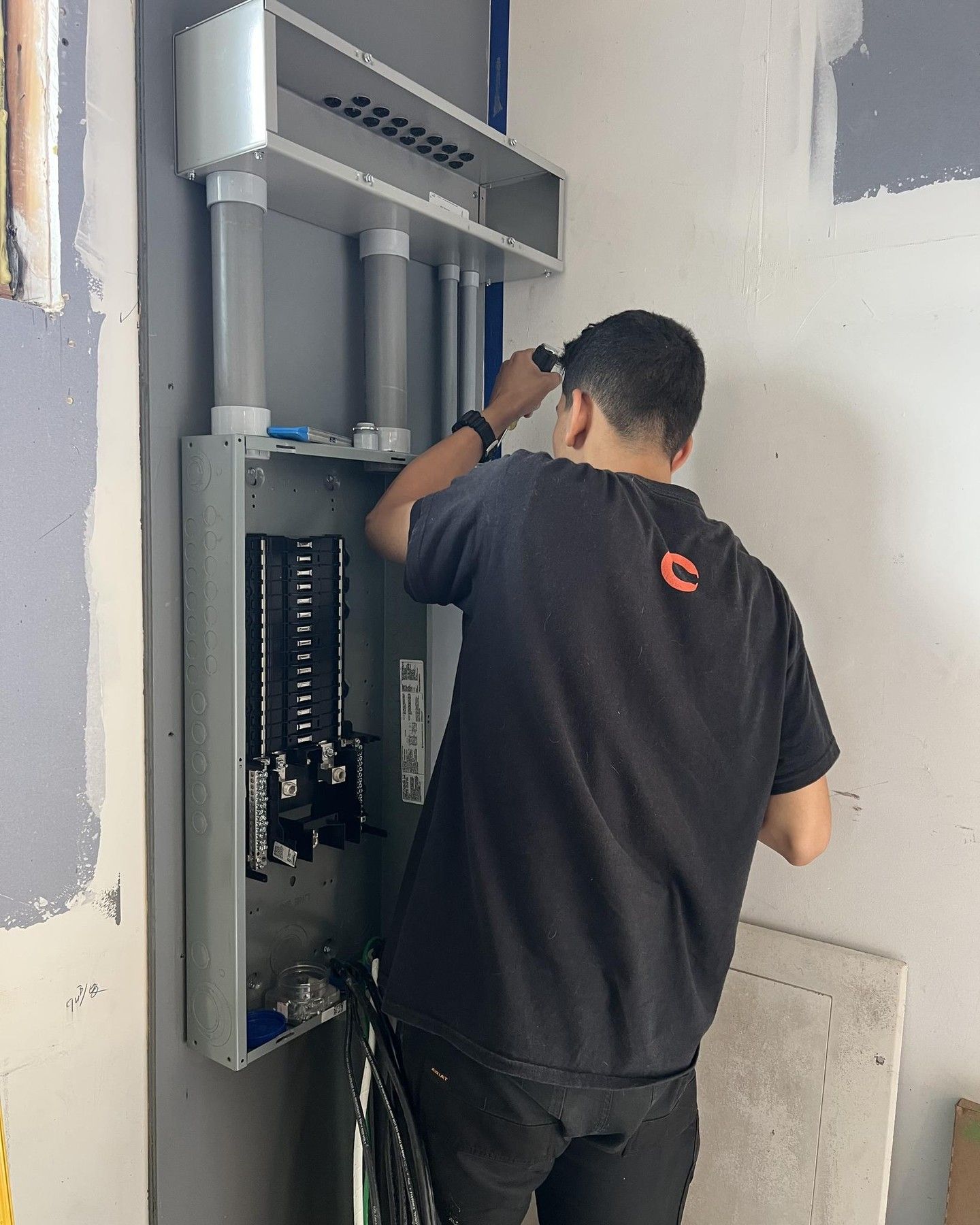 An electrician working on an electrical panel in a room with gray walls.