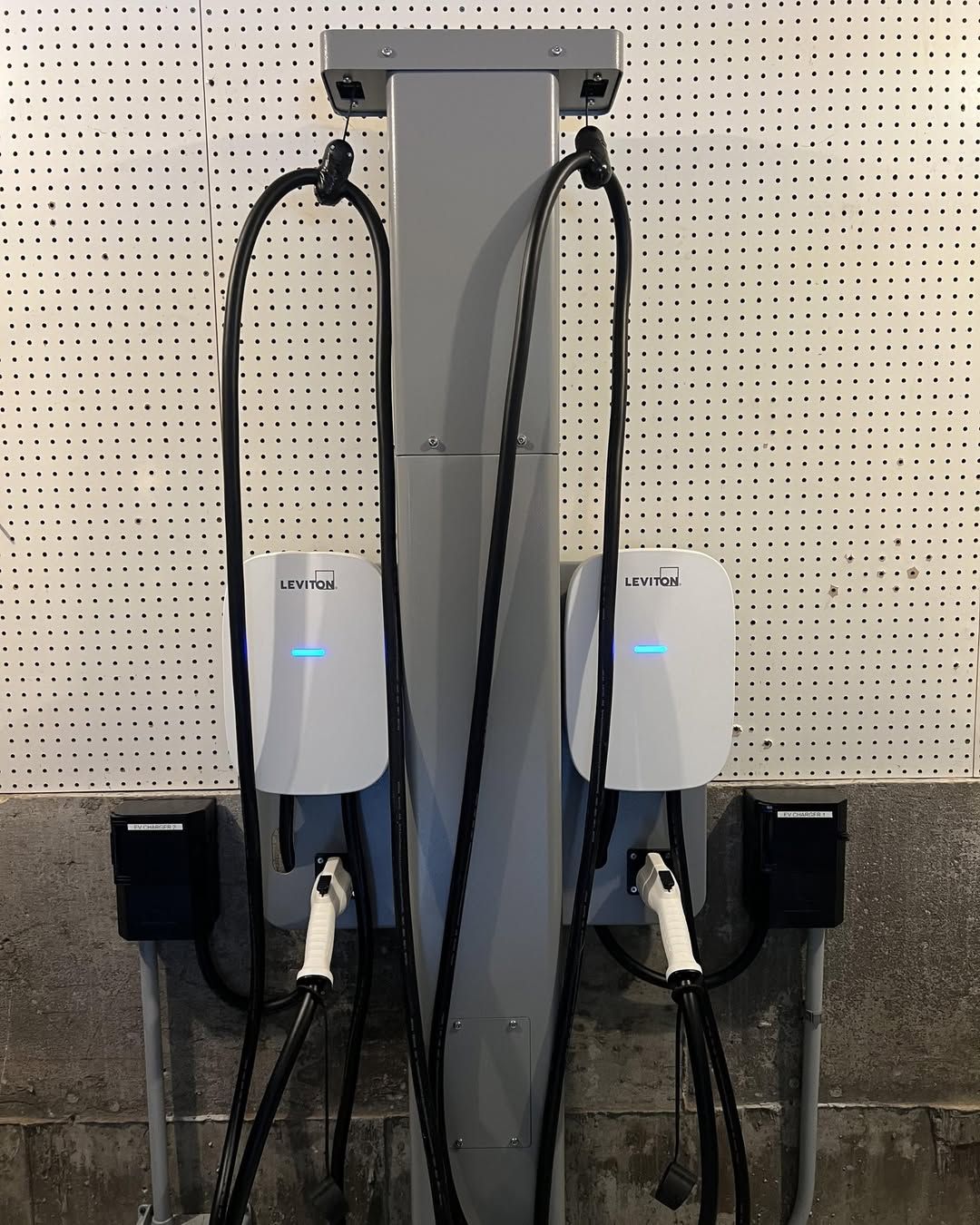 Electric vehicle charging station with two chargers, white with blue lights, black cords.