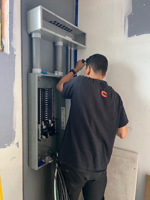 Electrician working on a gray electrical panel in a room with unfinished walls.