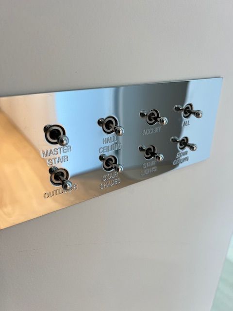 Shiny metal light switch panel with eight toggle switches labeled