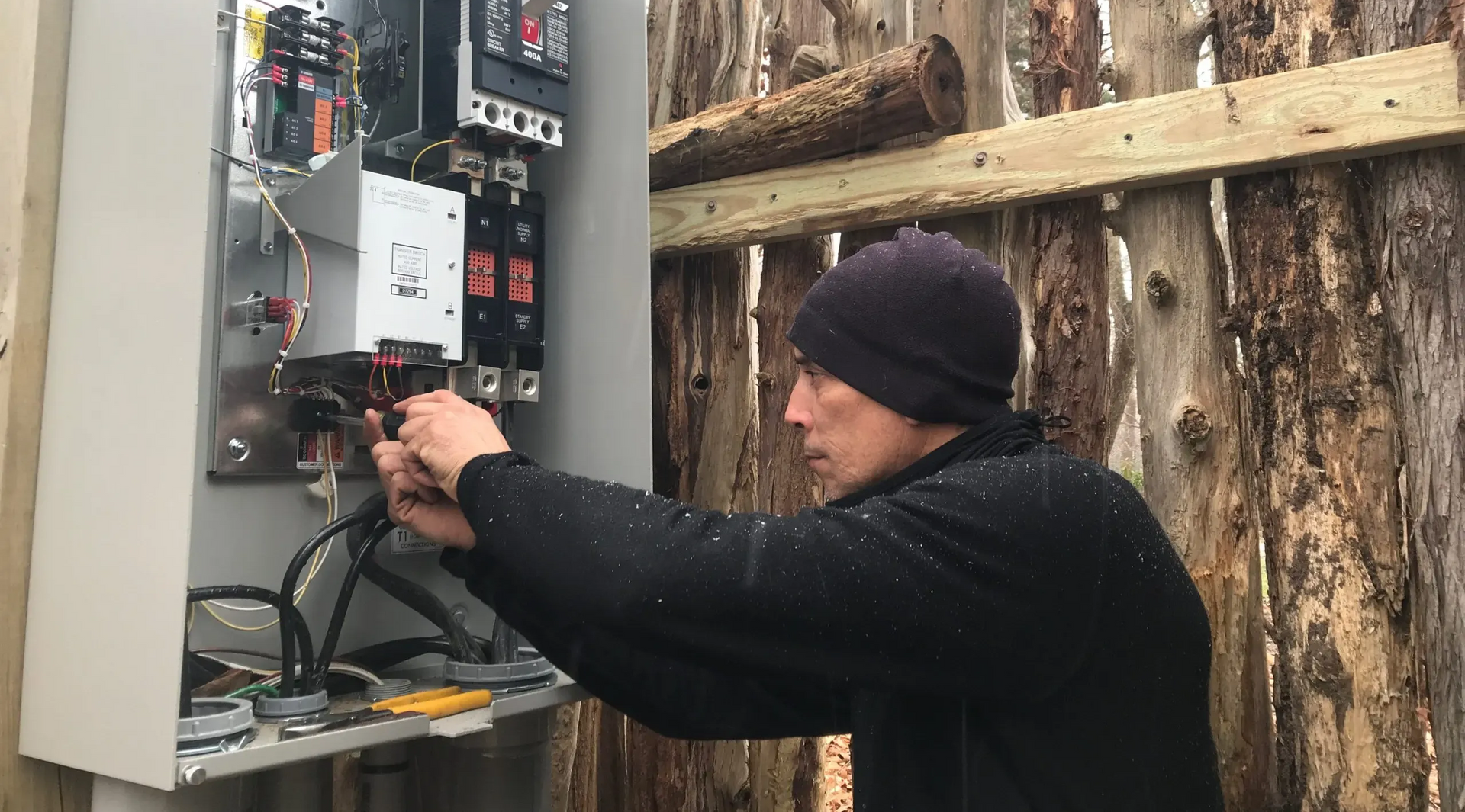 Person in black hat working on electrical panel outdoors.
