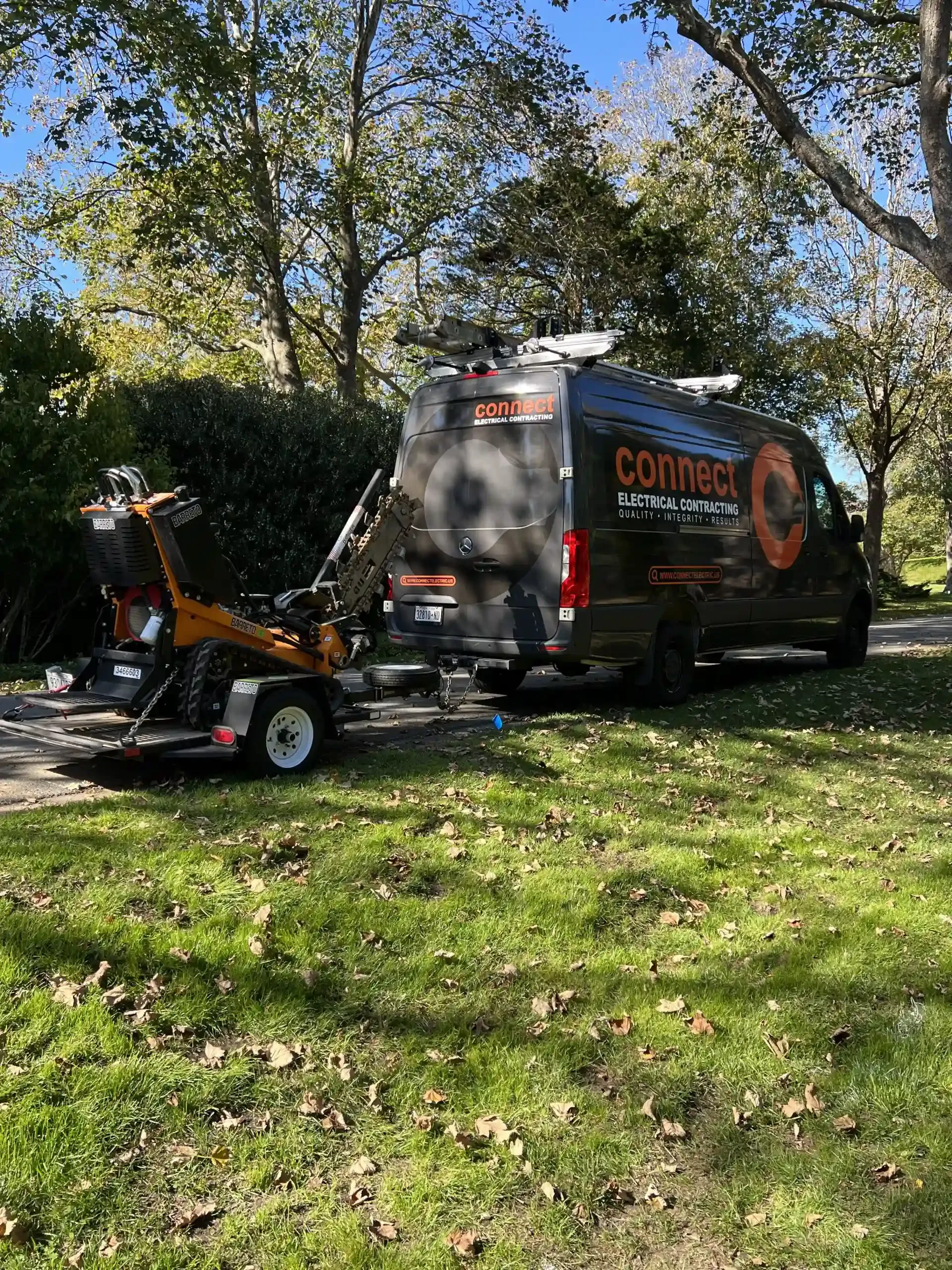 Black van with trailer and stump grinder parked on grassy area.