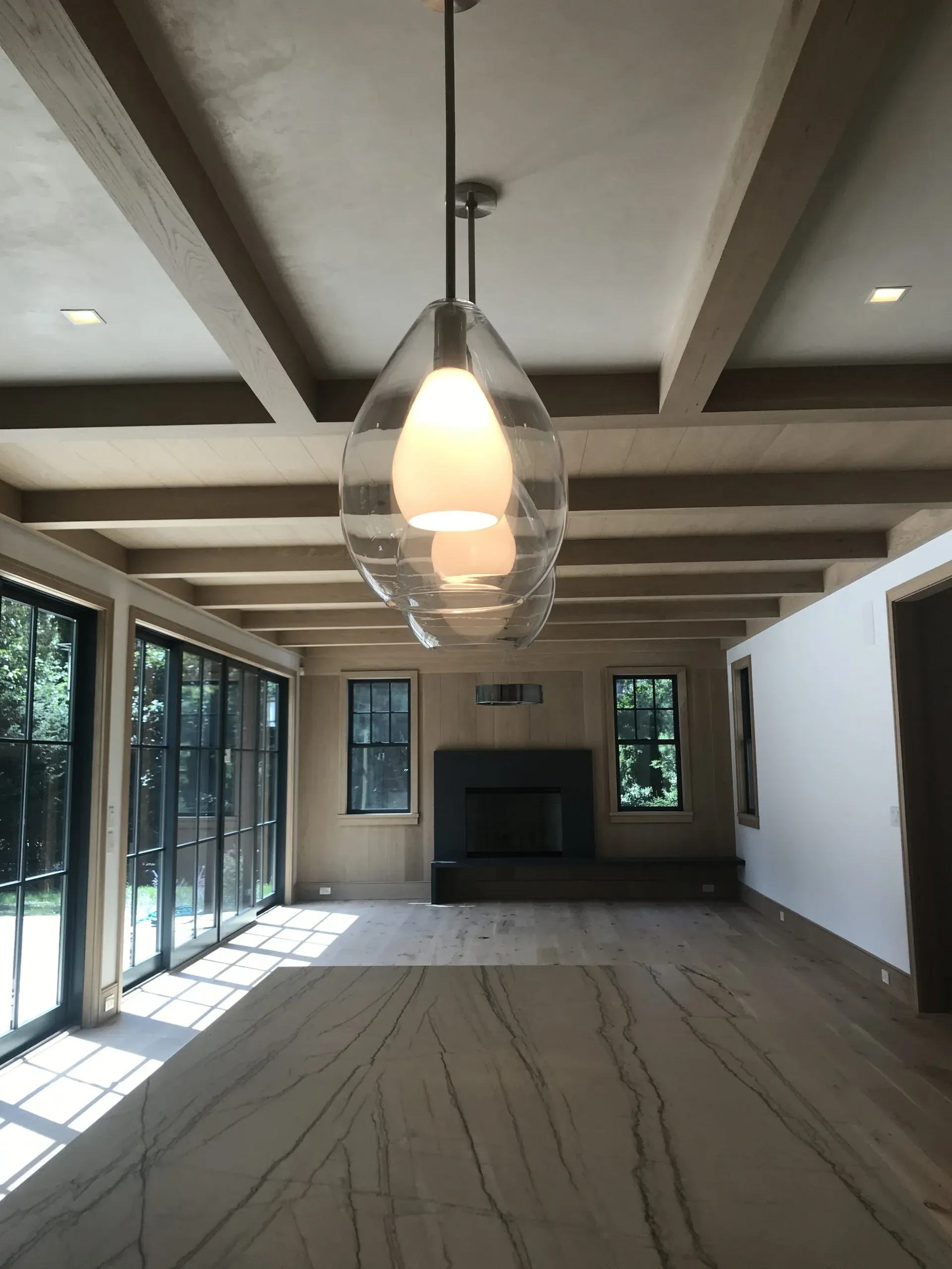 Spacious room with a fireplace, glass sliding doors, and a decorative light fixture hanging from the wood-beamed ceiling.