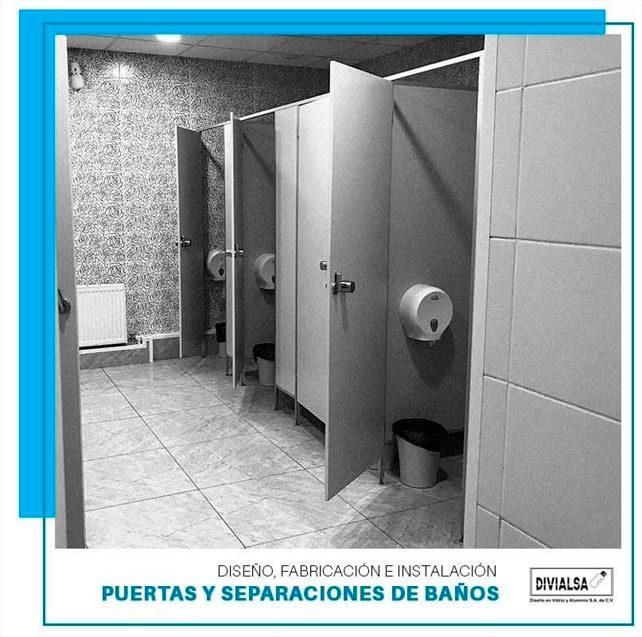 Baño público con cabinas blancas, dispensadores de jabón y papeleras.