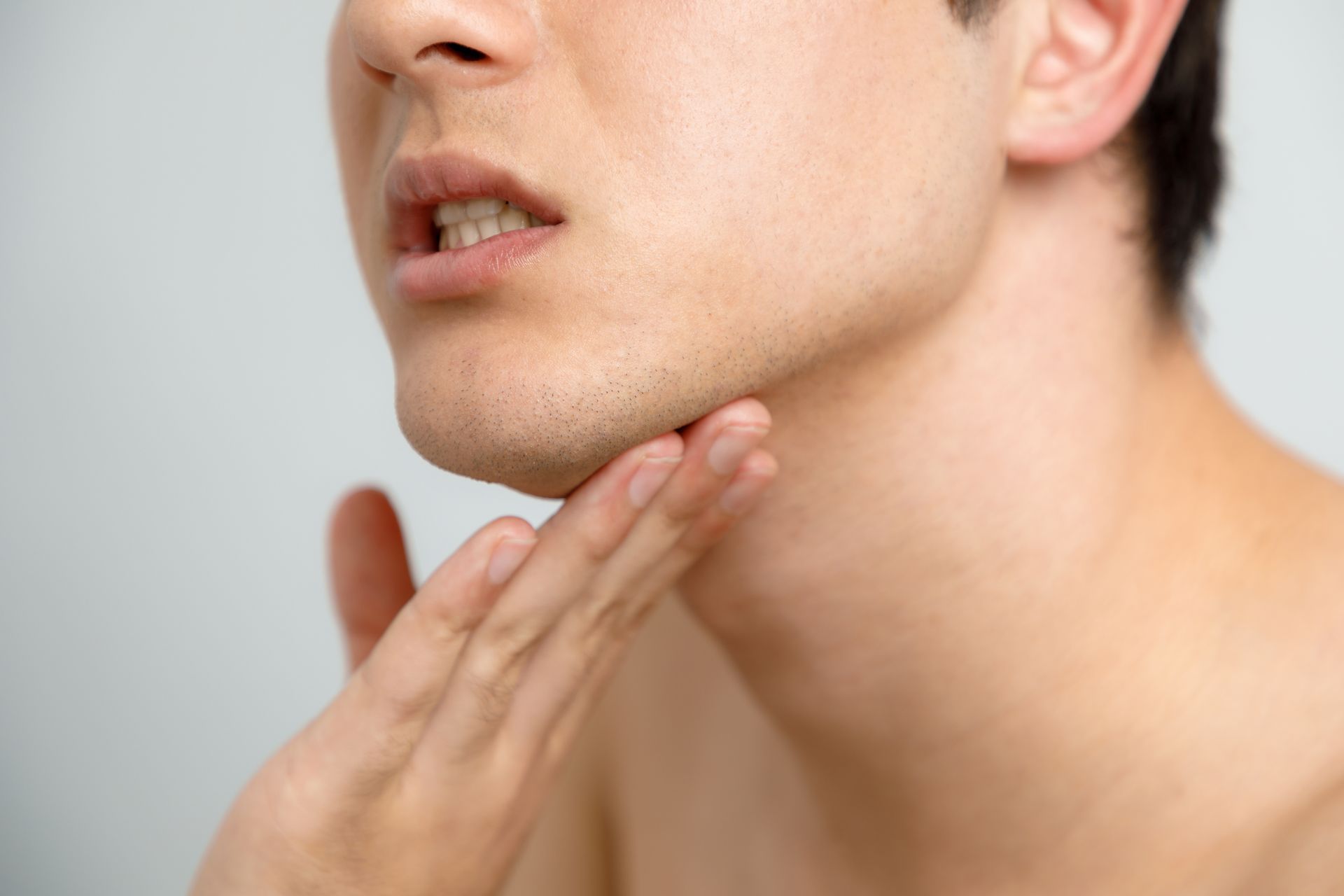 Man touching his jaw and neck. Shows part of his face, bare chest, indoors.