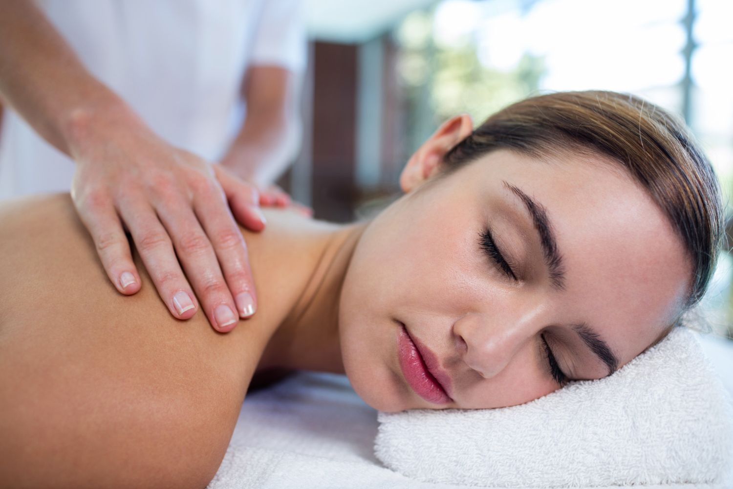 A person receiving a shoulder massage while resting face-down on a white towel