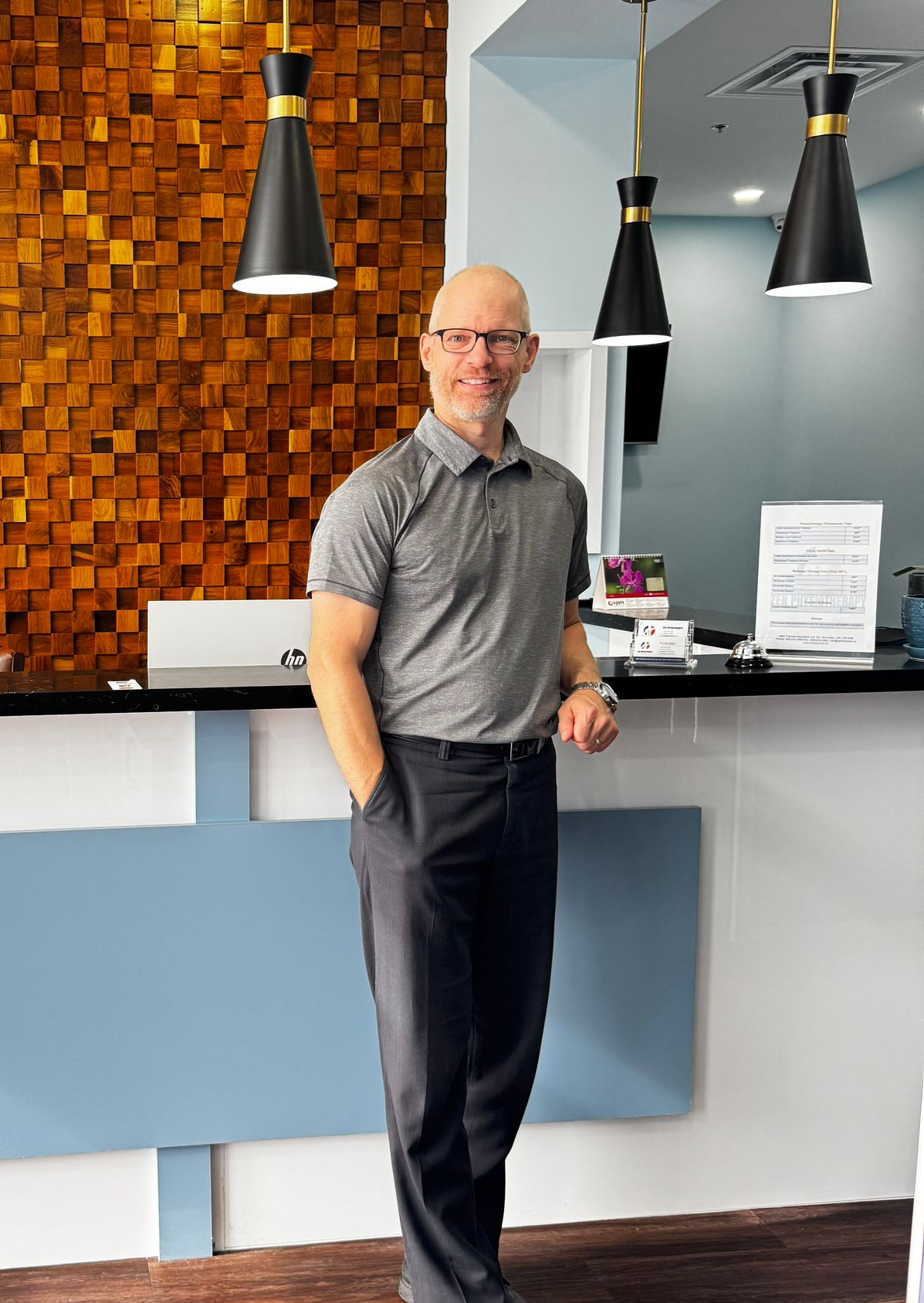 Man in a blue shirt smiling in a bright indoor setting with white blinds