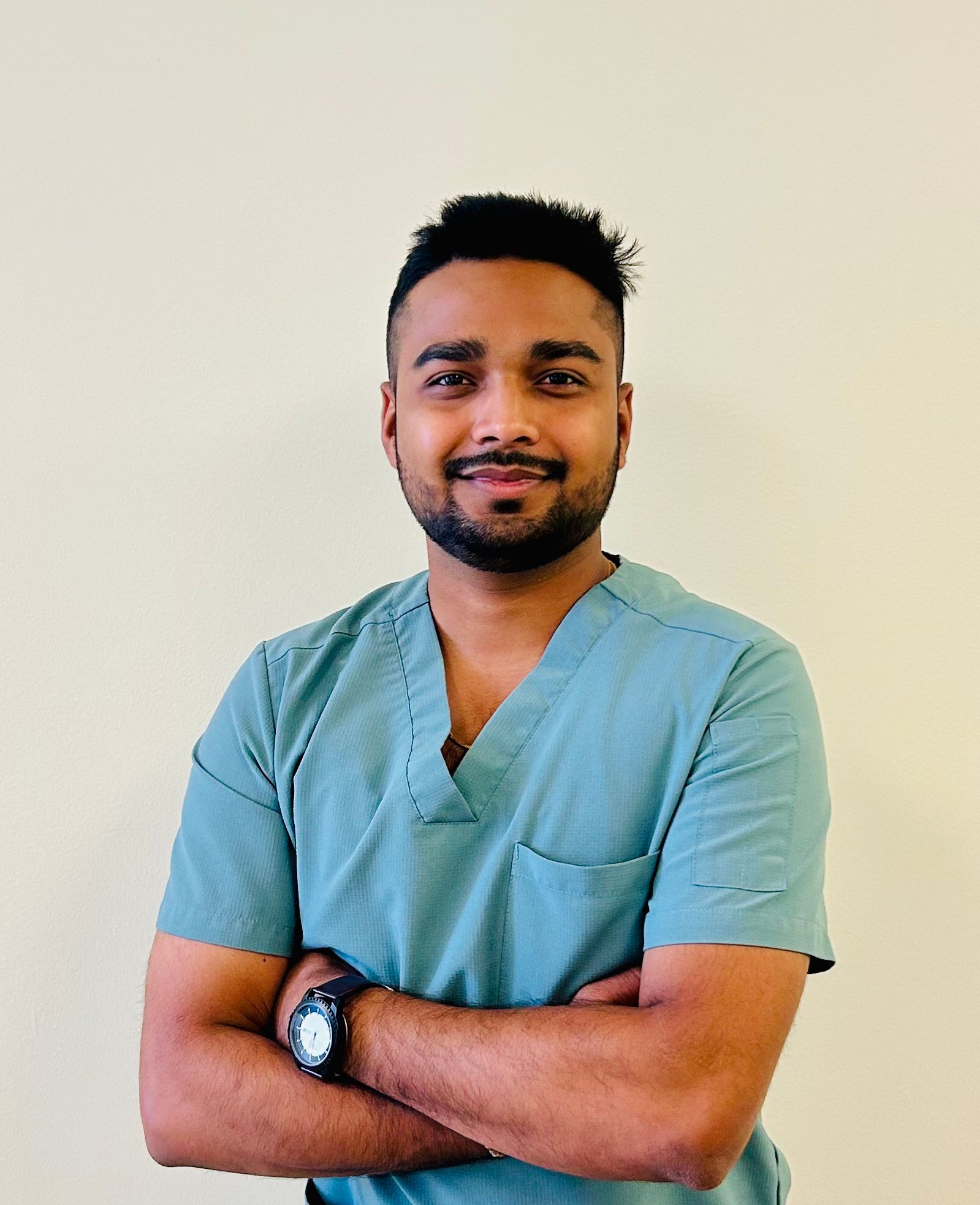 Person in teal medical scrubs stands with arms crossed against a plain light background.