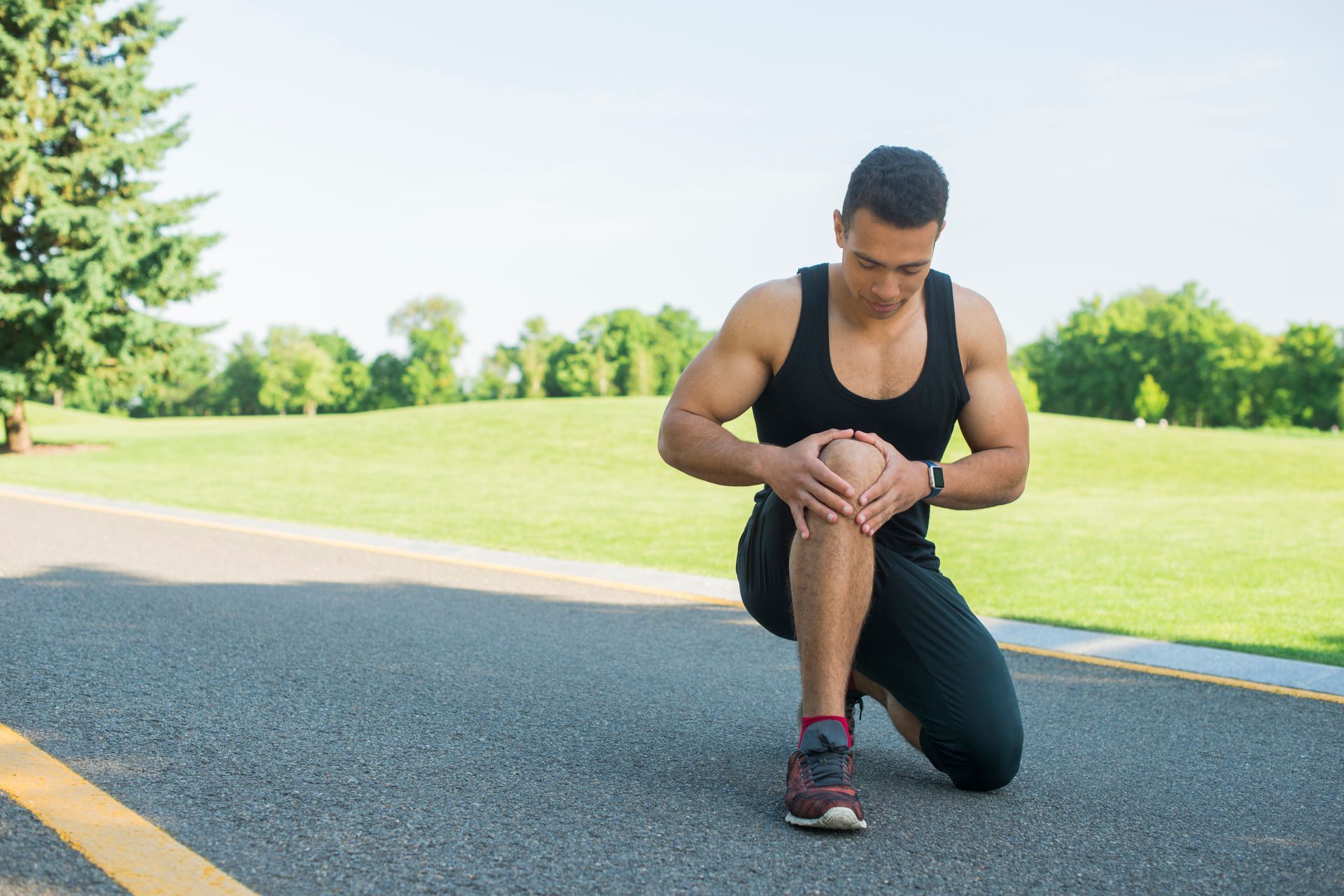 A man is kneeling down on the side of the road holding his knee.