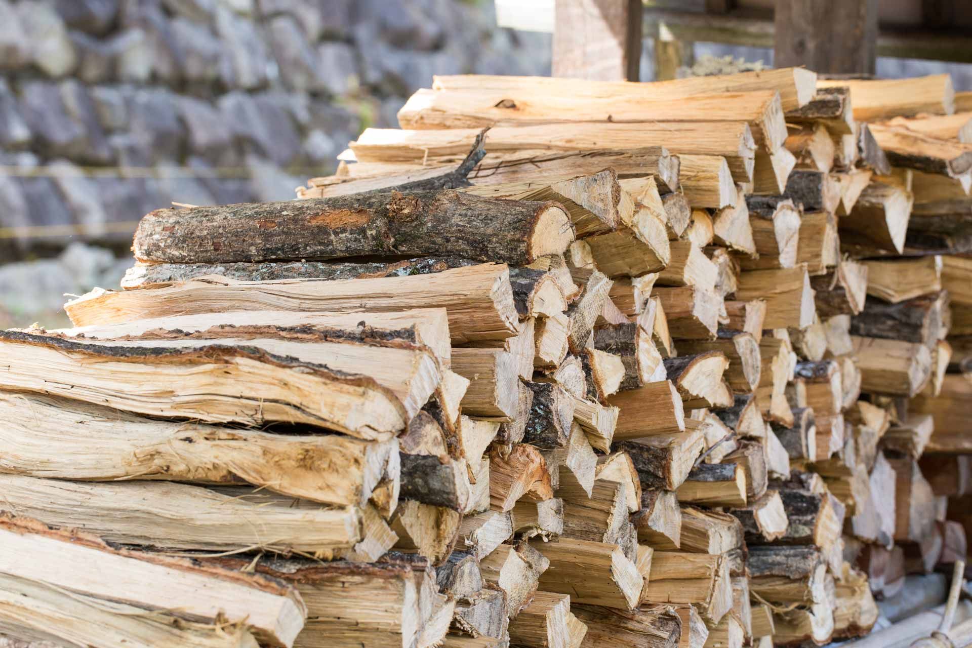 Stacked split firewood piled outdoors against a stone wall.
