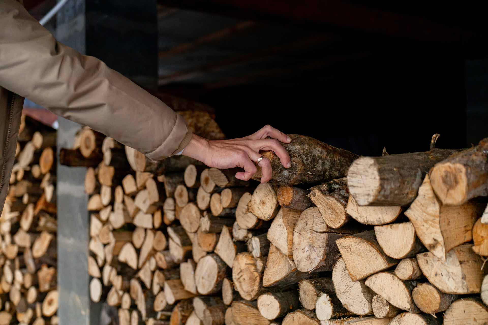 A hand resting on a stacked pile of split firewood in a dimly lit storage area