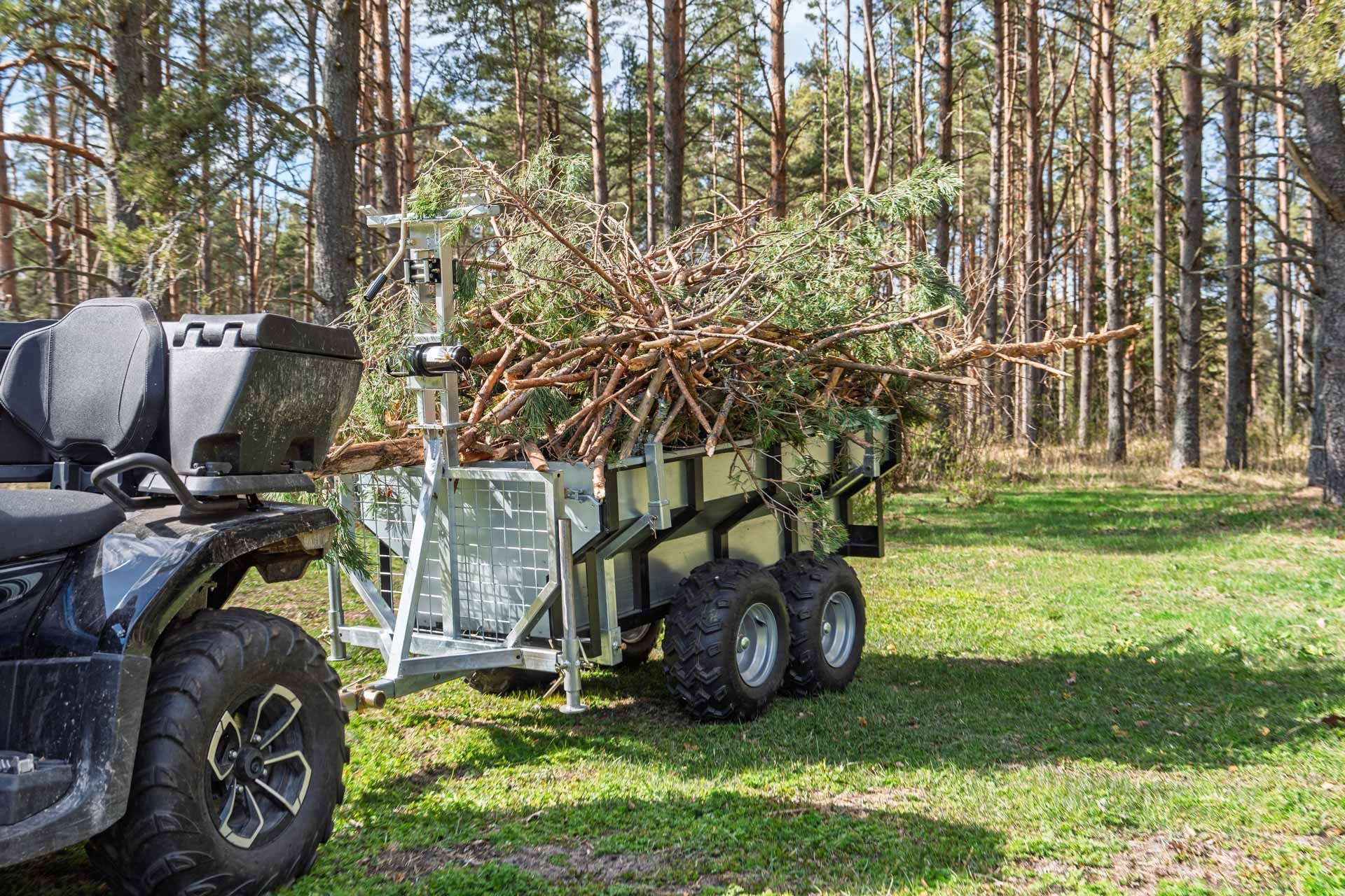 ATV towing a trailer loaded with branches in a grassy wooded area