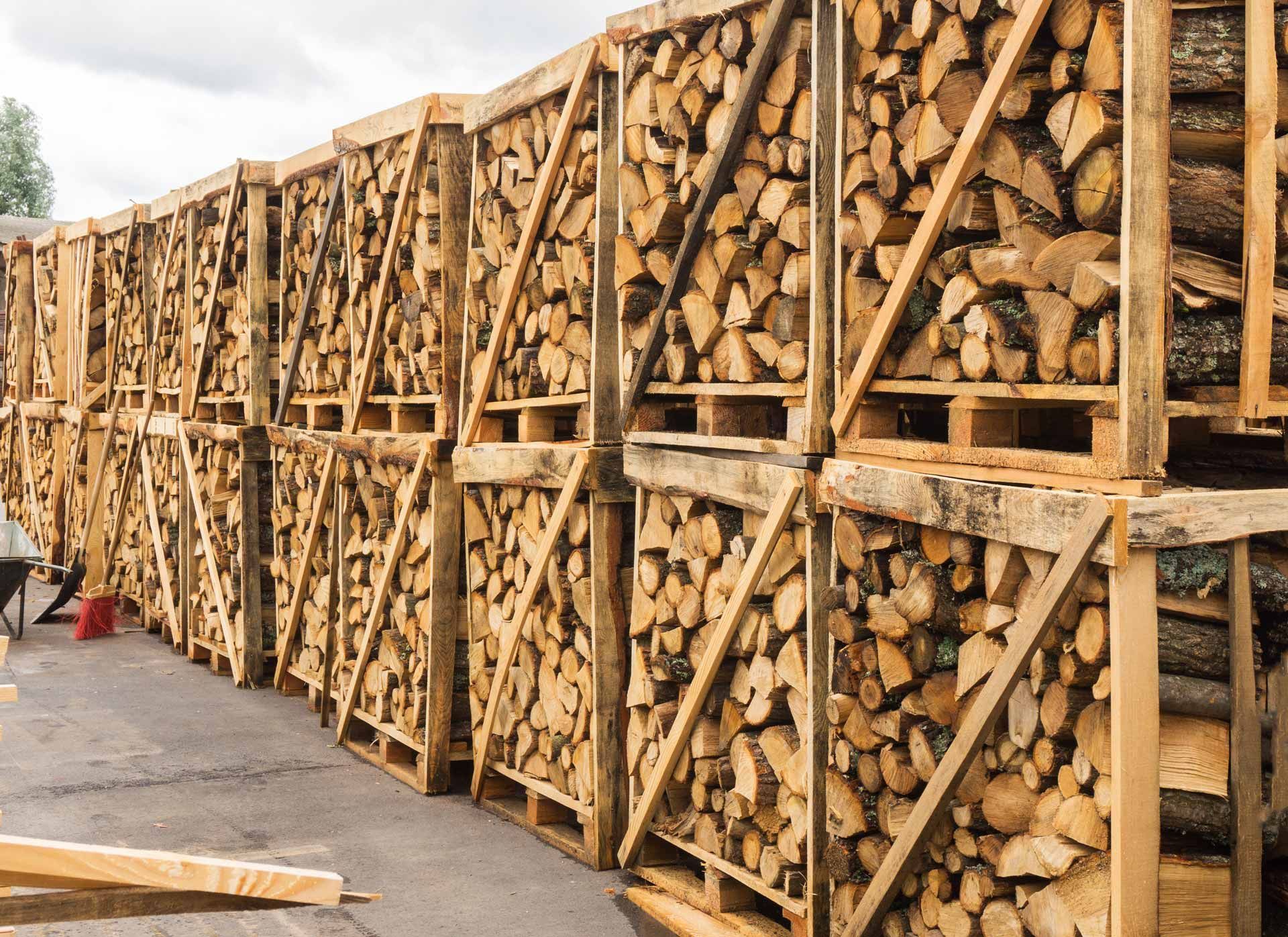 Rows of stacked firewood in wooden racks along an outdoor storage yard