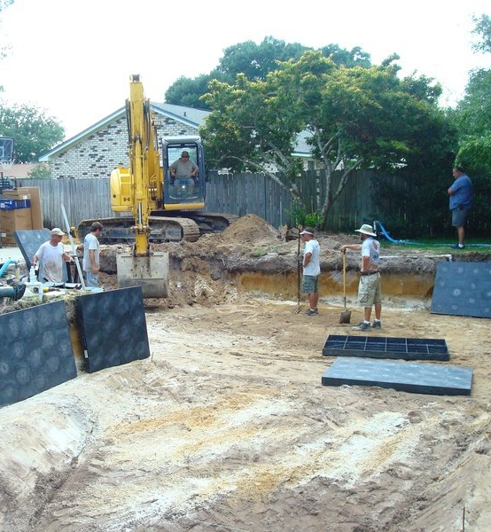 Construction site with an excavator digging; workers are installing black rectangular panels in a yard.