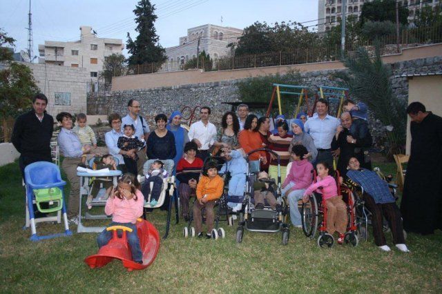 Gruppo di persone, alcune in sedia a rotelle, in un cortile con attrezzature da gioco.