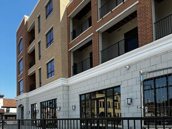 Multi-story brick building with balconies and large windows on a sunny day.
