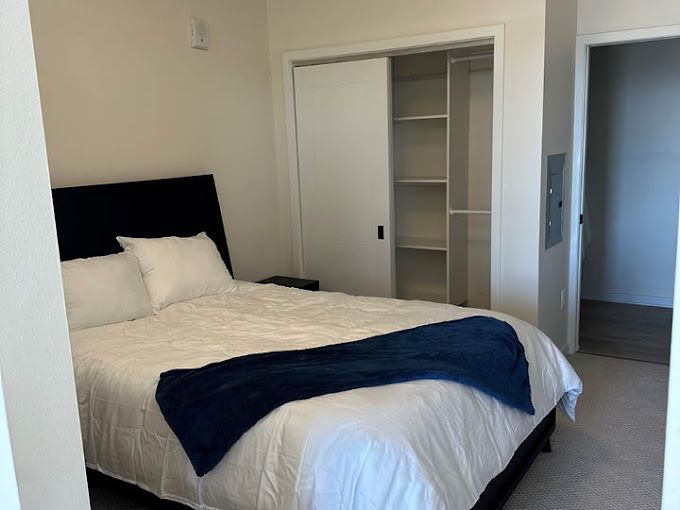 Bedroom with bed, closet, and open doorway, neutral tones, blue blanket.