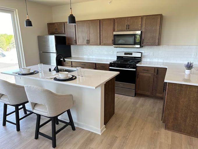 Modern kitchen with island, stainless steel appliances, brown cabinets, and white countertops.