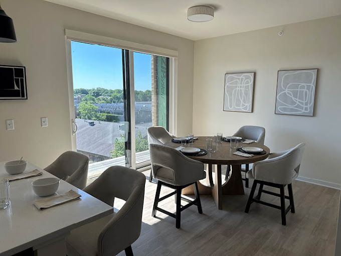 Dining room with round table, chairs, artwork, and large window overlooking a cityscape.