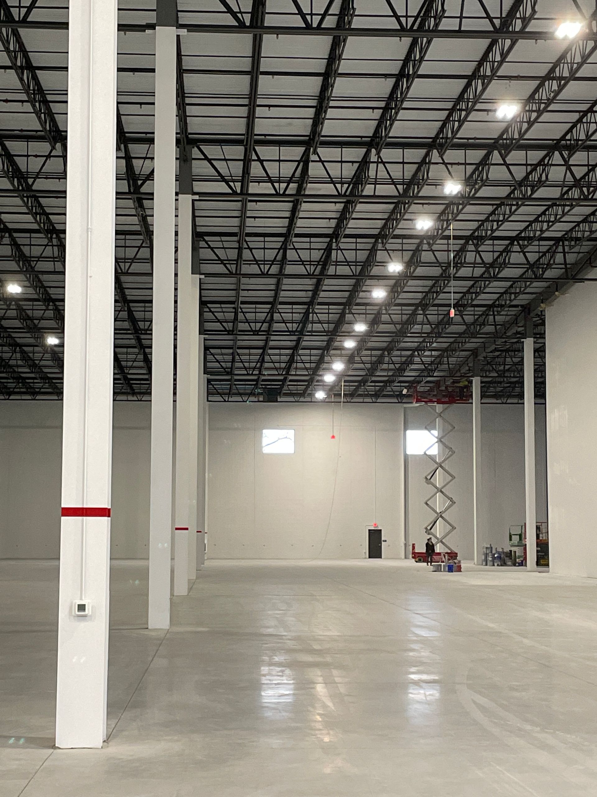 Empty industrial warehouse interior with high ceilings, white columns, and polished concrete floor