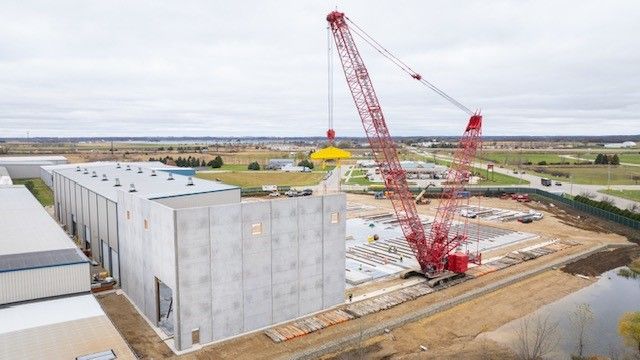 Red crane lifting object at a construction site near a large gray building.