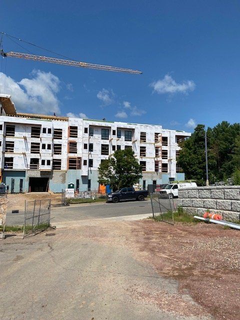 Construction of a multi-story building, exterior view. White siding, windows, and crane under a blue sky.