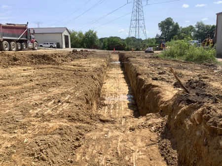 Construction site with long trench, brown dirt, and heavy machinery visible in the background.