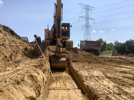 An excavator digging a trench at a construction site near a power line under a blue sky.