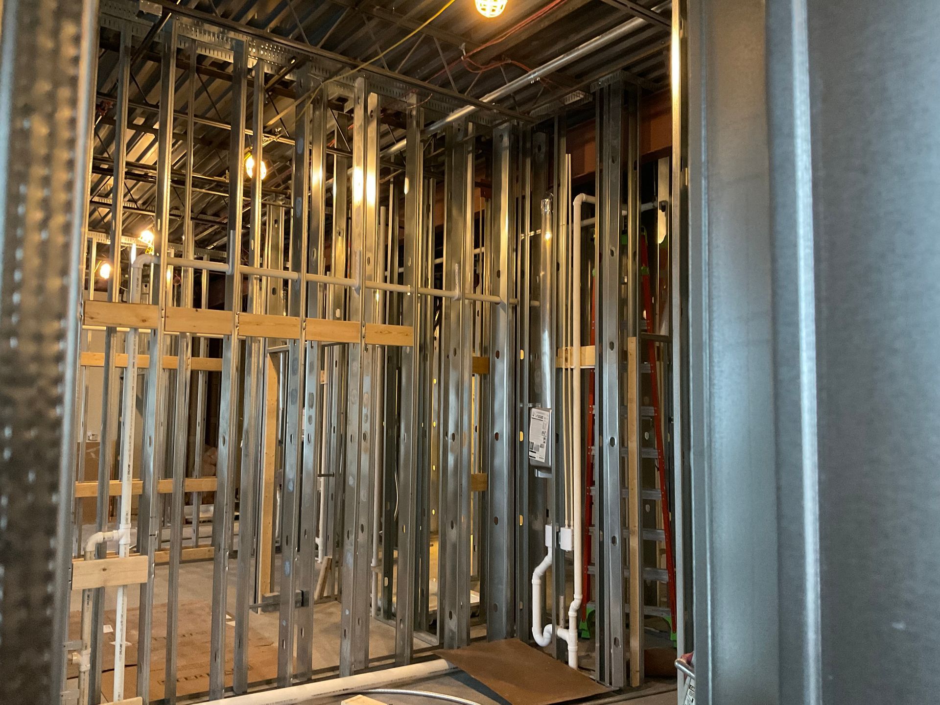 Interior of a room under construction, showing metal studs, exposed plumbing, and wooden framing.