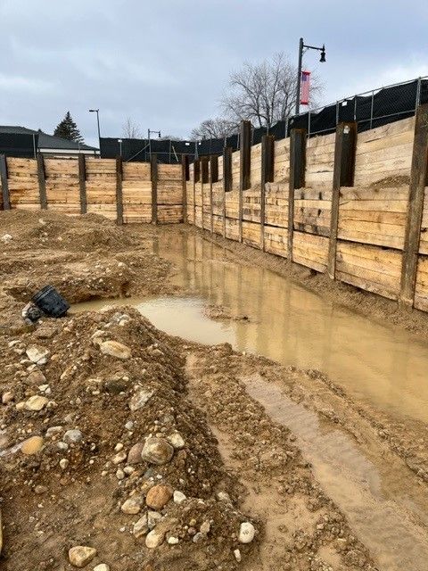 Construction site with wooden retaining wall and muddy ground with standing water.
