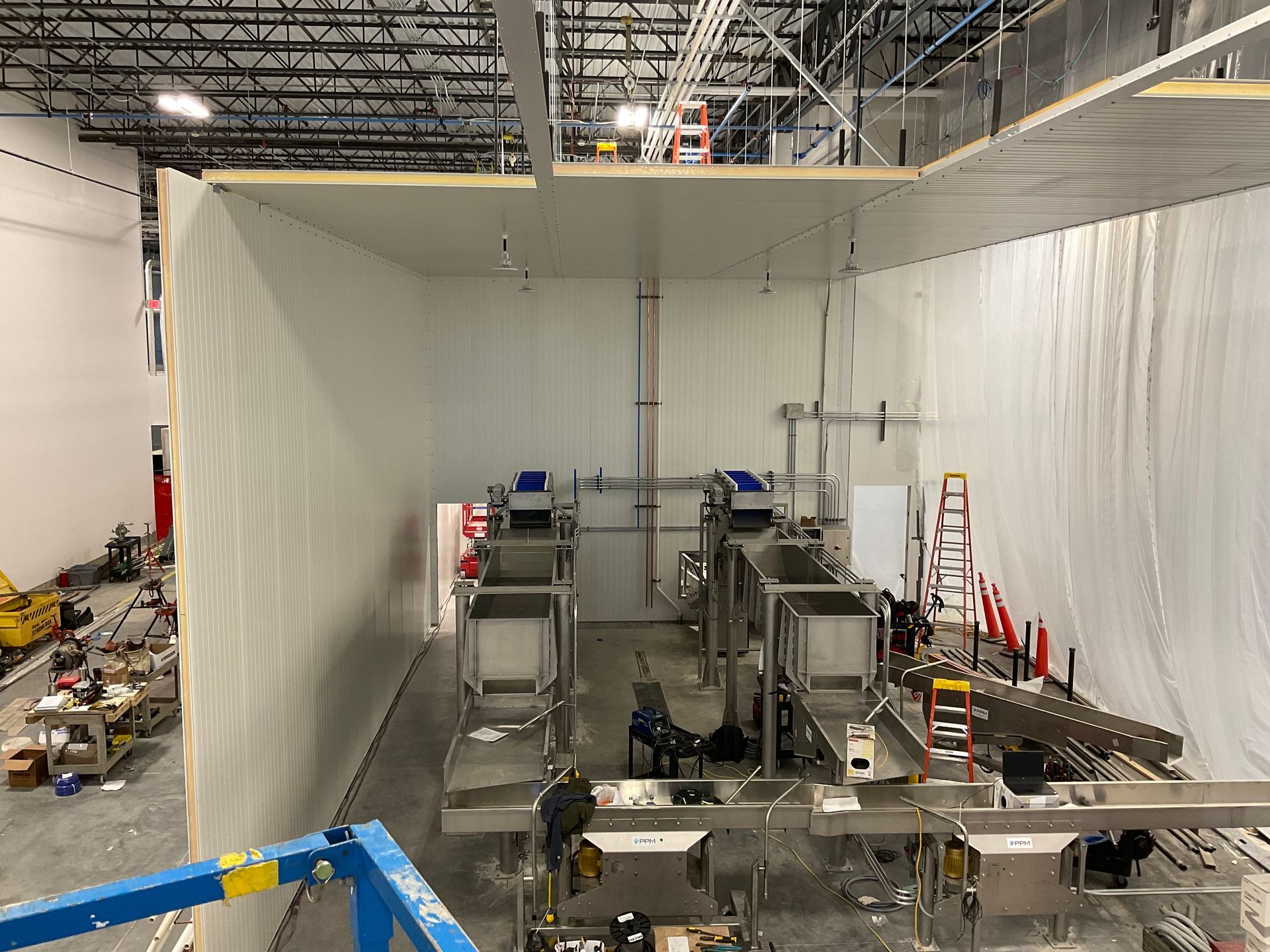 Interior view of a food processing room under construction, with stainless steel equipment and white walls.